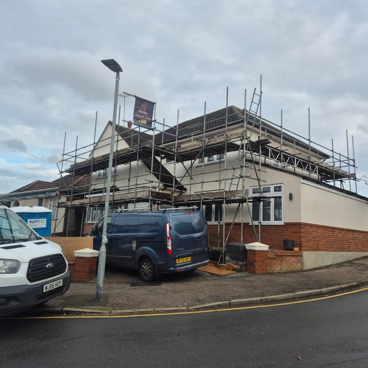 Devlins branded van parked in front of a semi-detached house with scaffolding banner