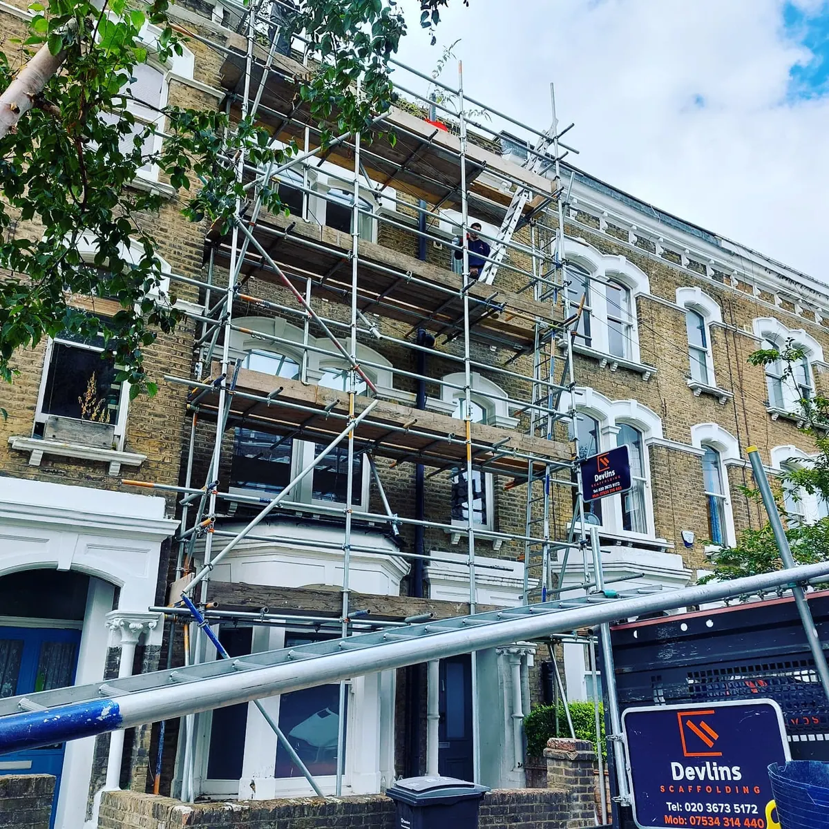 Devlins branded van parked outside a Victorian multi-storey terrace with a purple scaffolding board