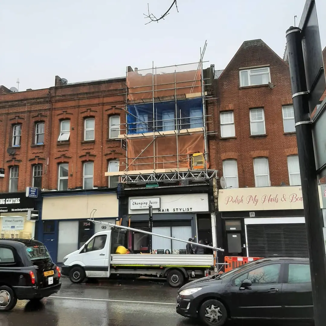 Commercial scaffolding on a redbrick building, rainy North London street with truck and black cab