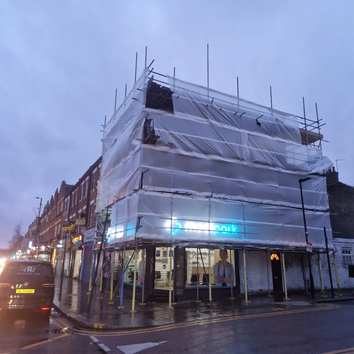 Devlins Scaffolding encapsulation on a North London corner shop at dusk in the rain