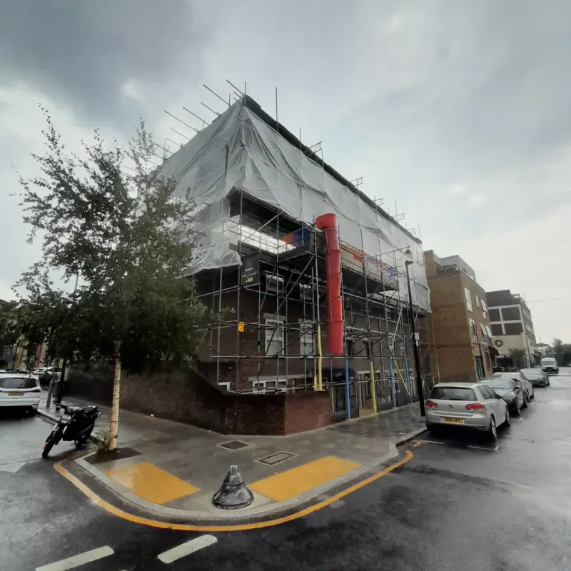 Full encapsulation scaffolding on a corner building with red waste chute in the rain